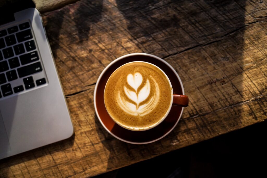 caffe latte i vit keramikkopp bredvid silver och svart bärbar dator